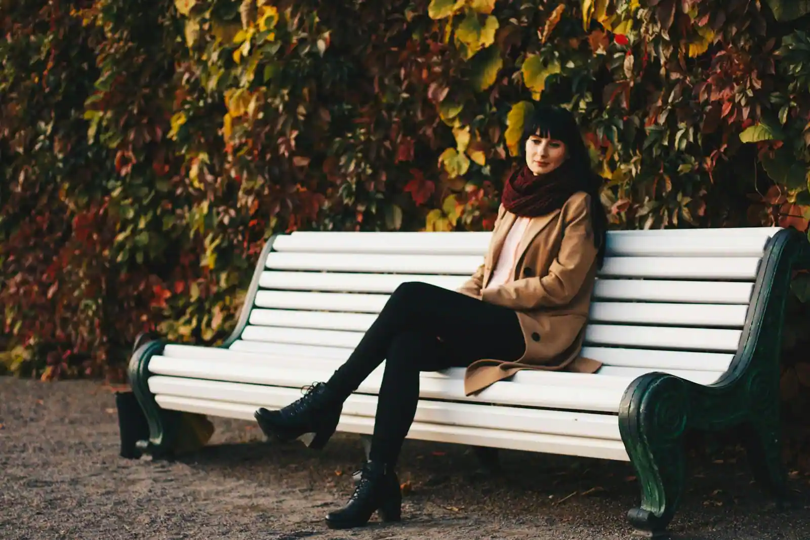 Silhouette mode automne-hiver avec manteau long bordeaux et bottes hautes en cuir dans une rue parisienne
