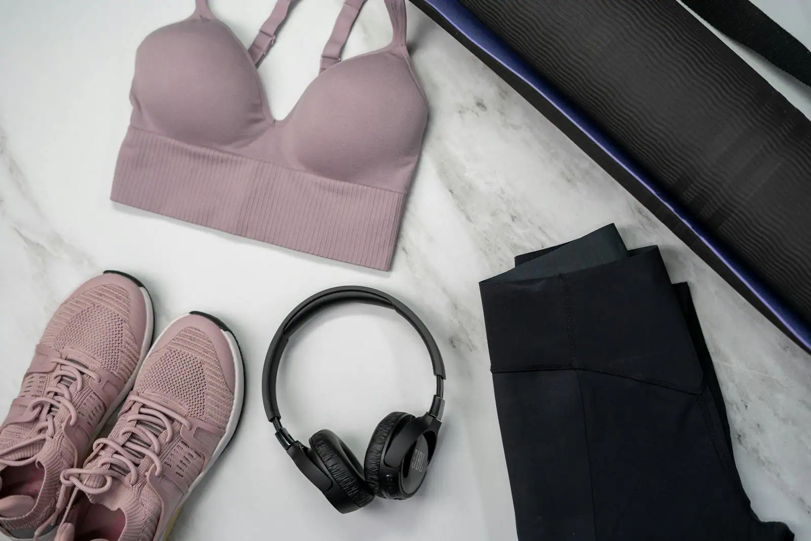 Vêtements de sport techniques étalés : brassière, legging, tee-shirt respirant et chaussures running sur fond clair