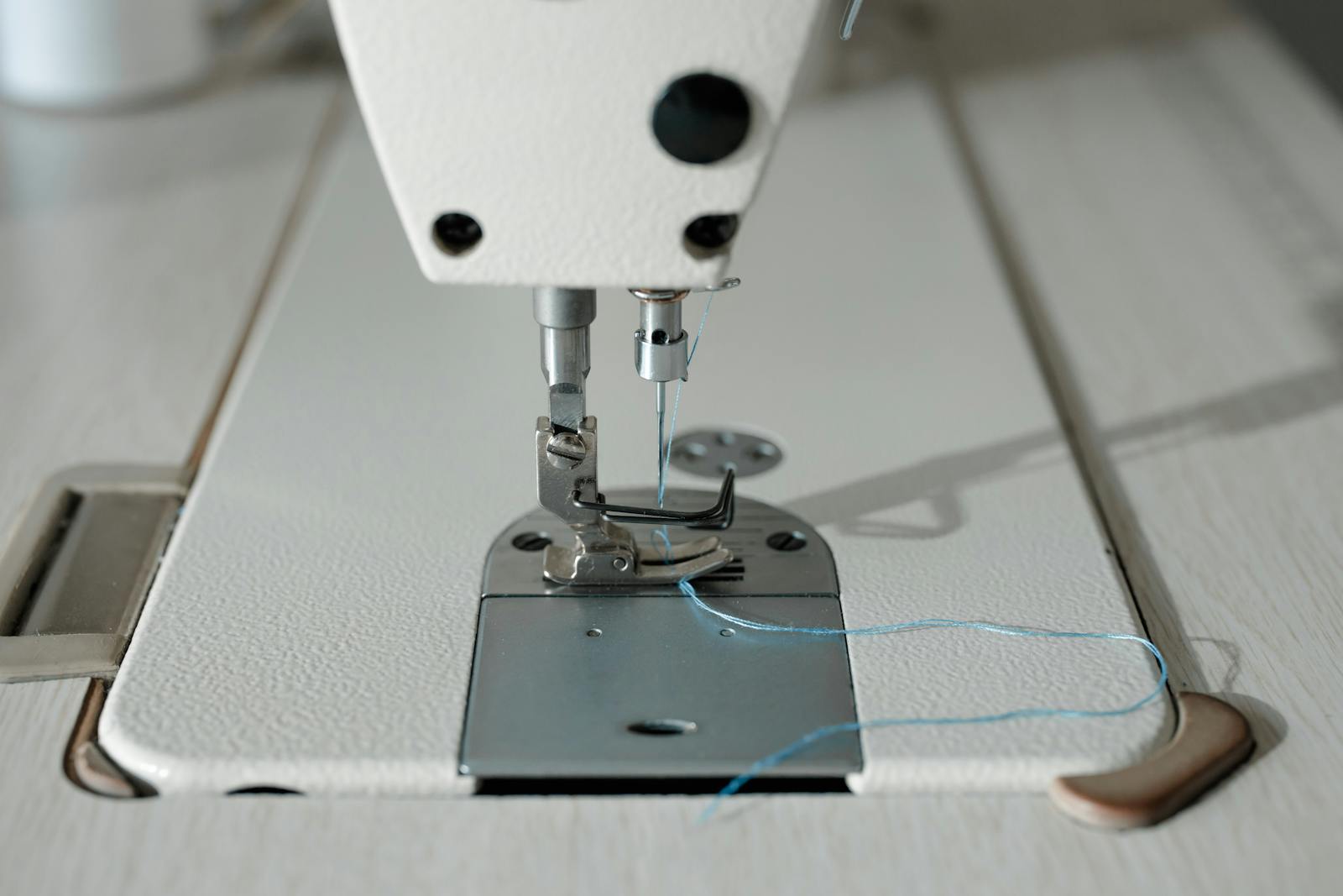 Machine à coudre moderne ouverte sur un plan de travail clair, bobines de fil colorées et tissus rangés à proximité.