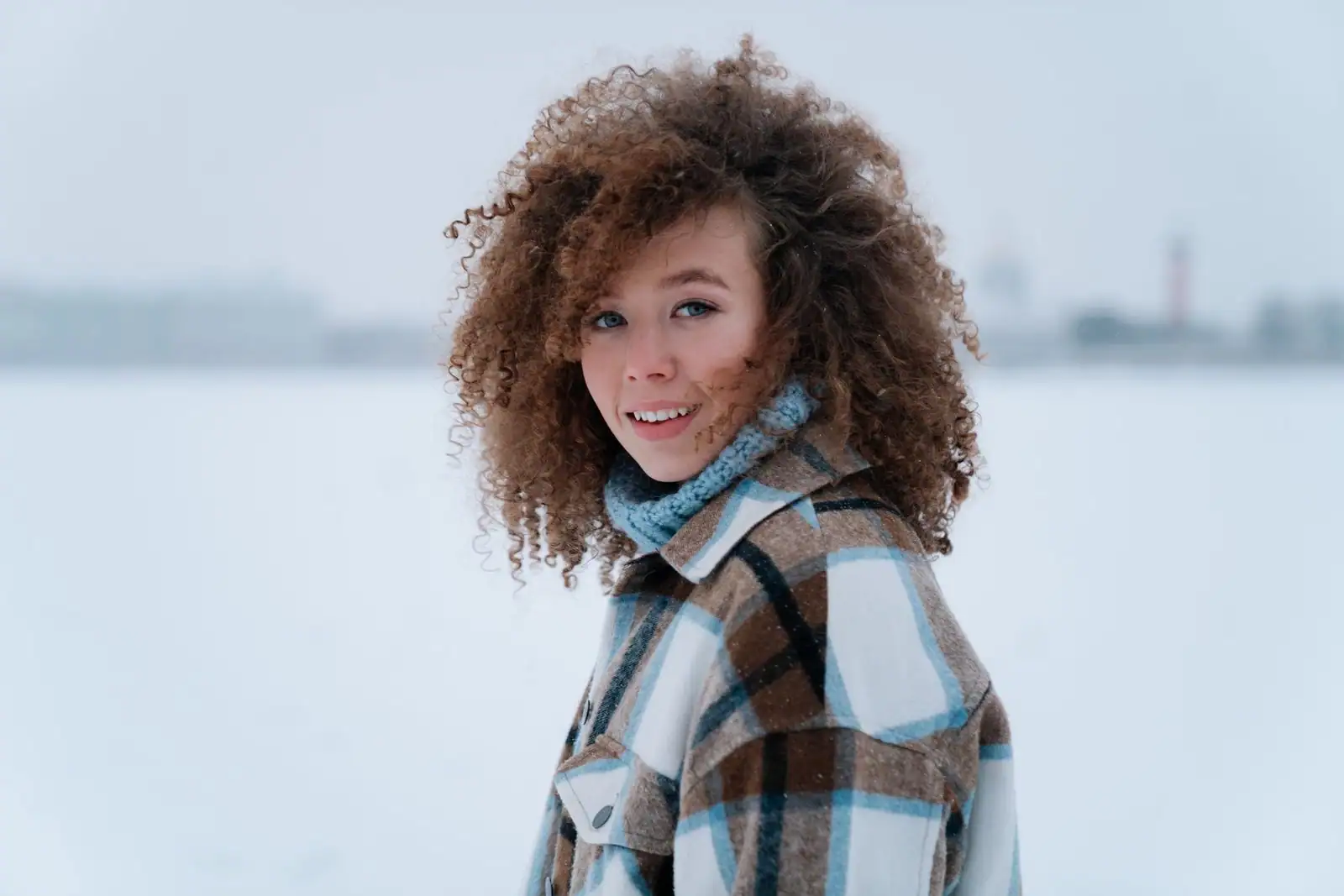 Jeune femme souriante aux cheveux bouclés, volumineux et bien définis, en extérieur l'hiver.