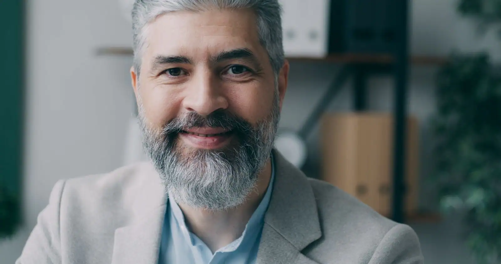 Homme souriant aux cheveux et à la barbe poivre et sel, mèches grises mêlées aux cheveux foncés