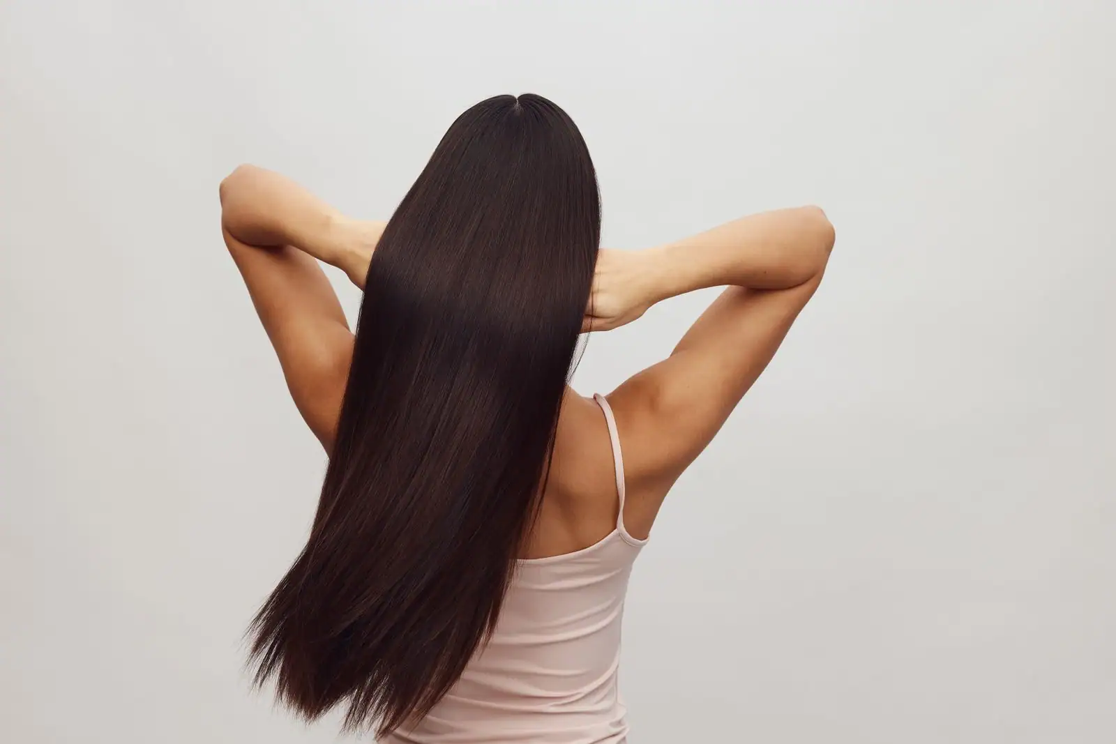 Femme vue de dos aux longs cheveux raides, lisses et brillants, mains relevant les longueurs