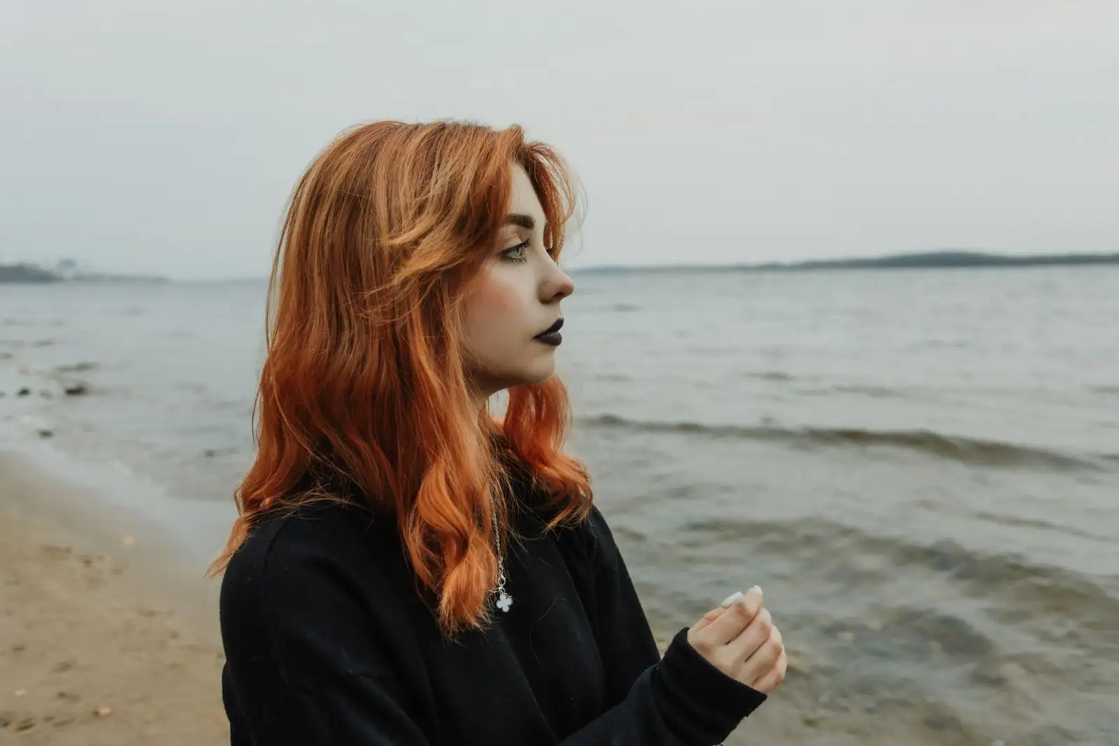 Femme aux longs cheveux roux cuivrés au bord de la mer, sous une lumière naturelle douce