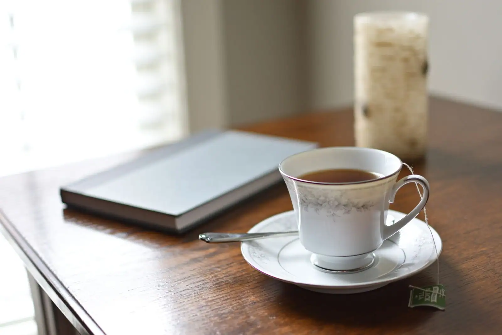 Livre fermé à couverture claire et tasse de thé sur une table en bois sombre, dans une ambiance feutrée de lecture