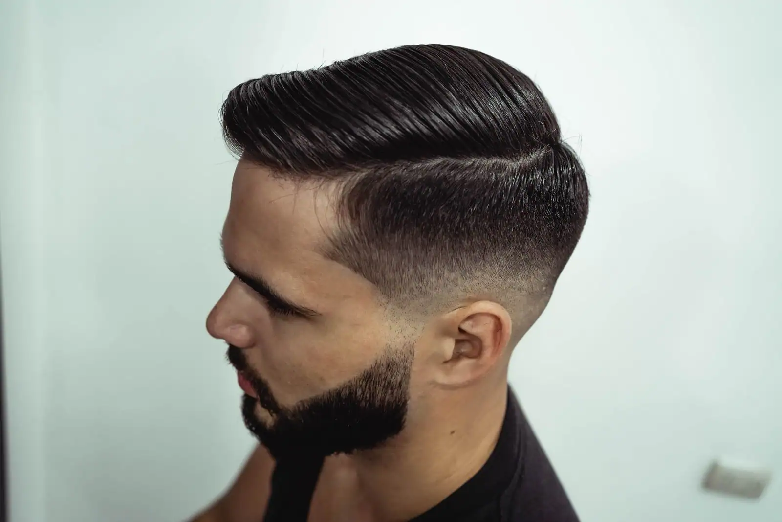 Homme de profil, cheveux courts coiffés sur le côté avec un dégradé et barbe taillée