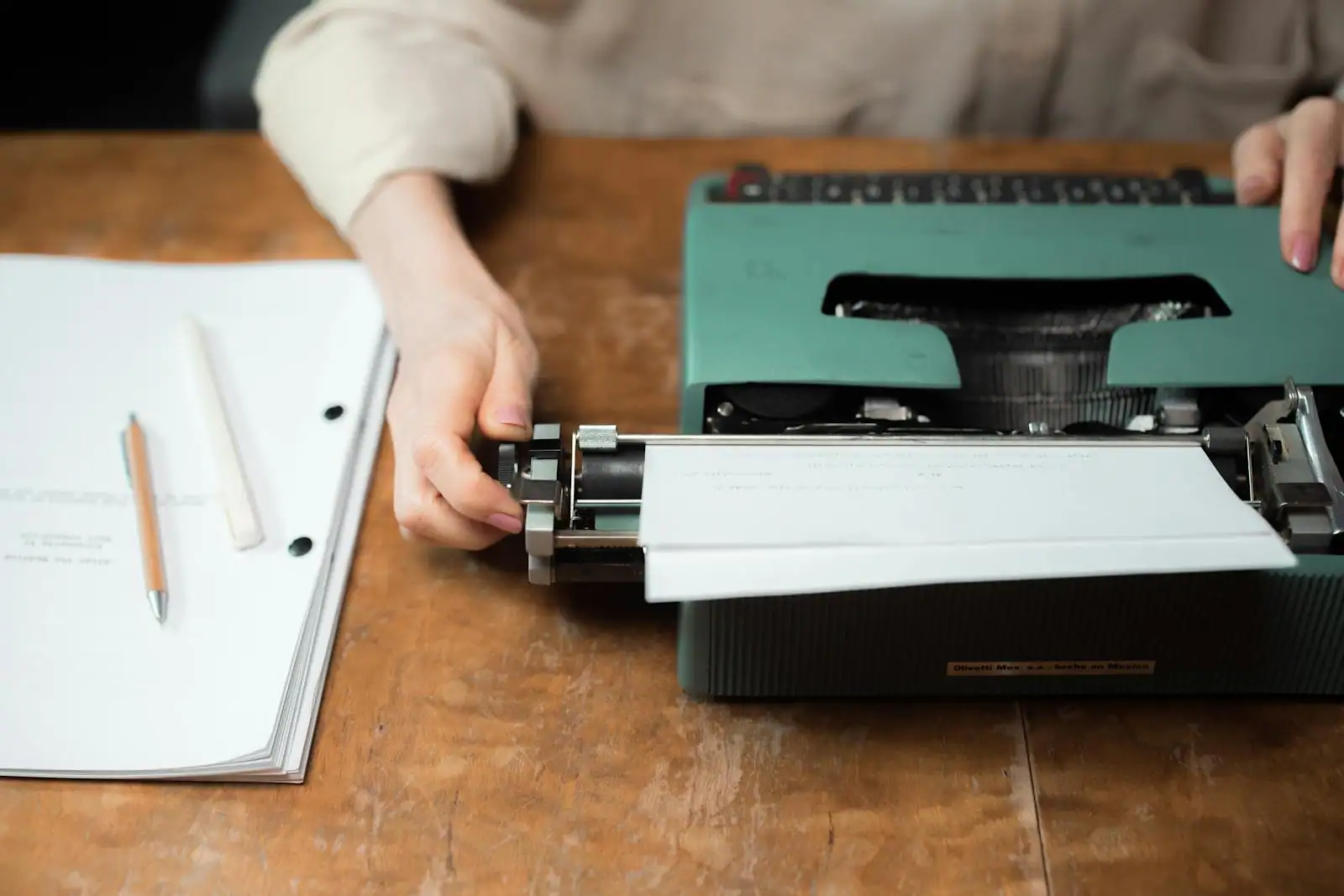 Mains tapant sur une machine à écrire vintage, manuscrit posé sur un bureau en bois