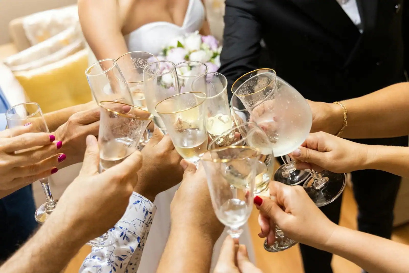 Mains levées trinquant avec des coupes de champagne lors d'un mariage, mariés en arrière-plan