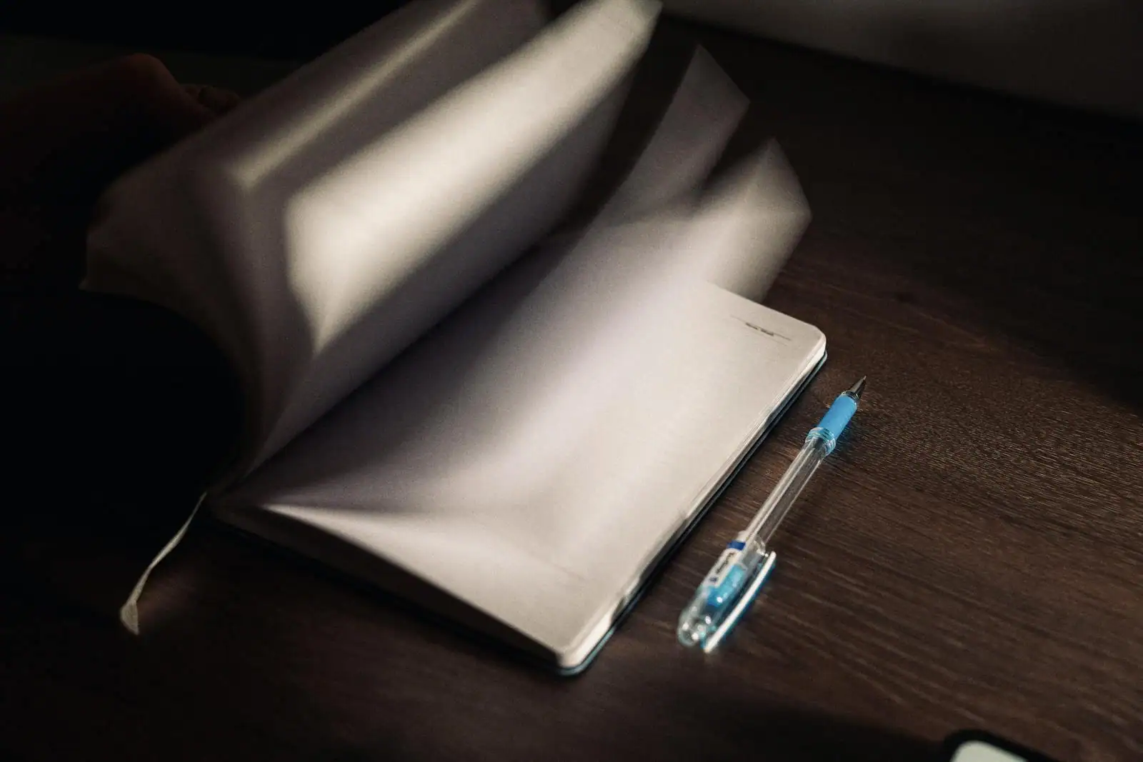 Carnet ouvert et stylo bleu posés sur un bureau en bois, dans une lumière tamisée