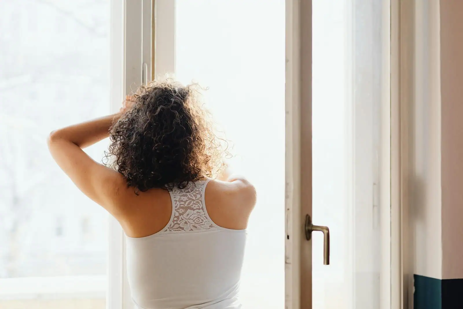 Femme debout près d'une fenêtre, baignée d'une lumière douce, dans un moment de calme