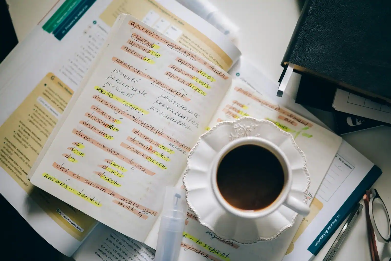Des notes manuscrites de vocabulaire d'une langue étrangère, surlignées, posées près d'une tasse de café et de manuels