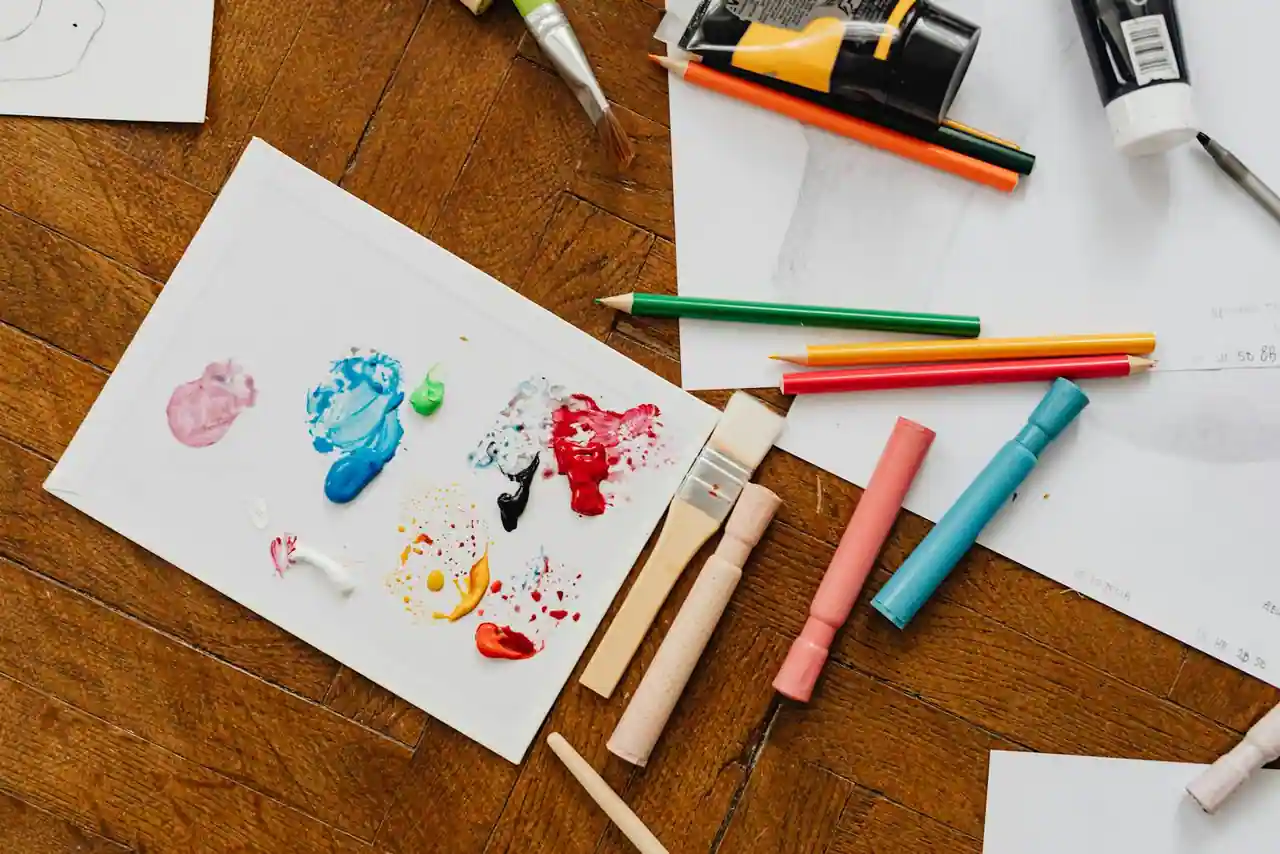 Vue de dessus de matériel de loisirs créatifs — pinceaux, crayons de couleur et peinture — sur une surface en bois.