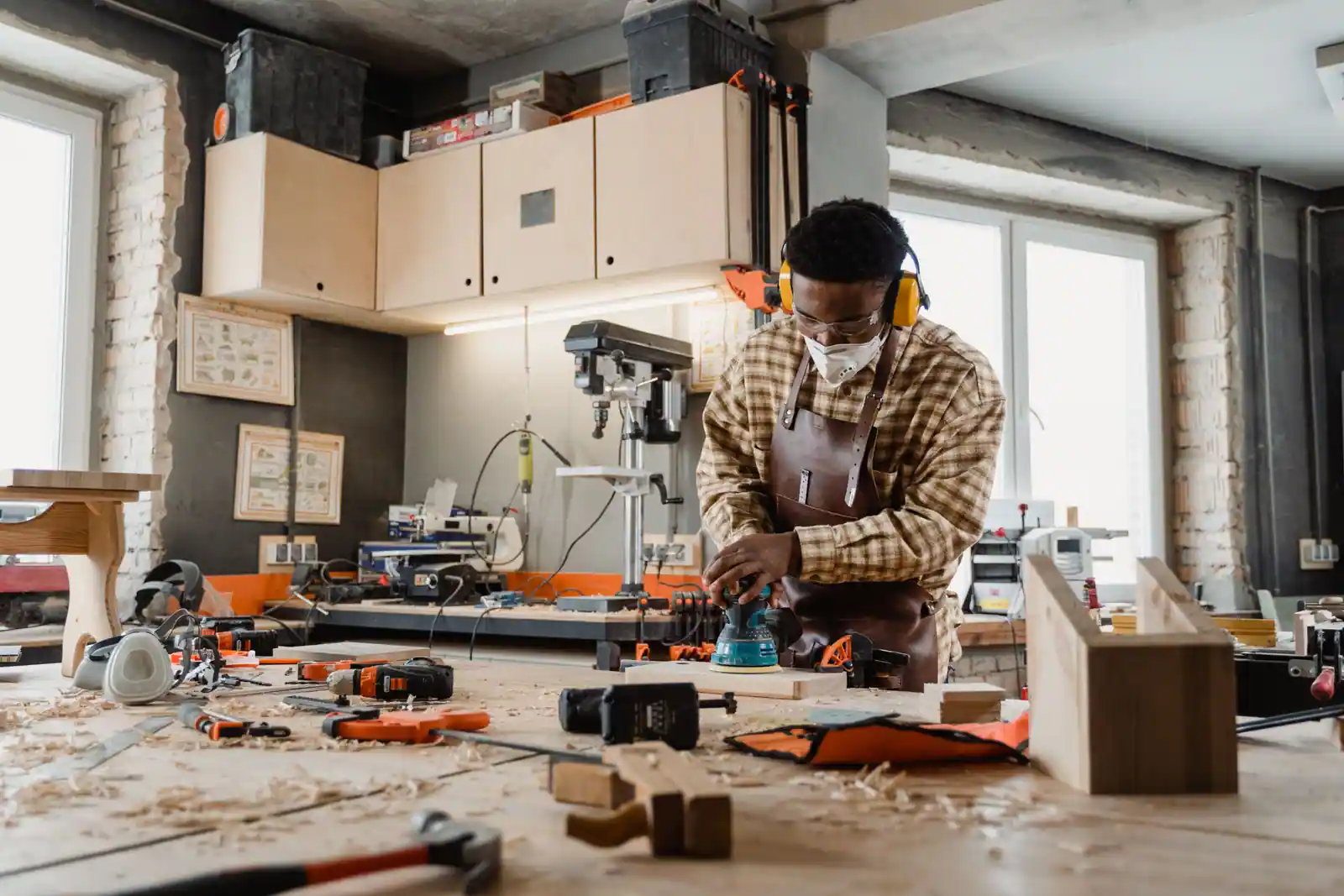 Un homme équipé de lunettes et d'un casque ponce une pièce de bois dans son atelier, illustration d'un hobby manuel