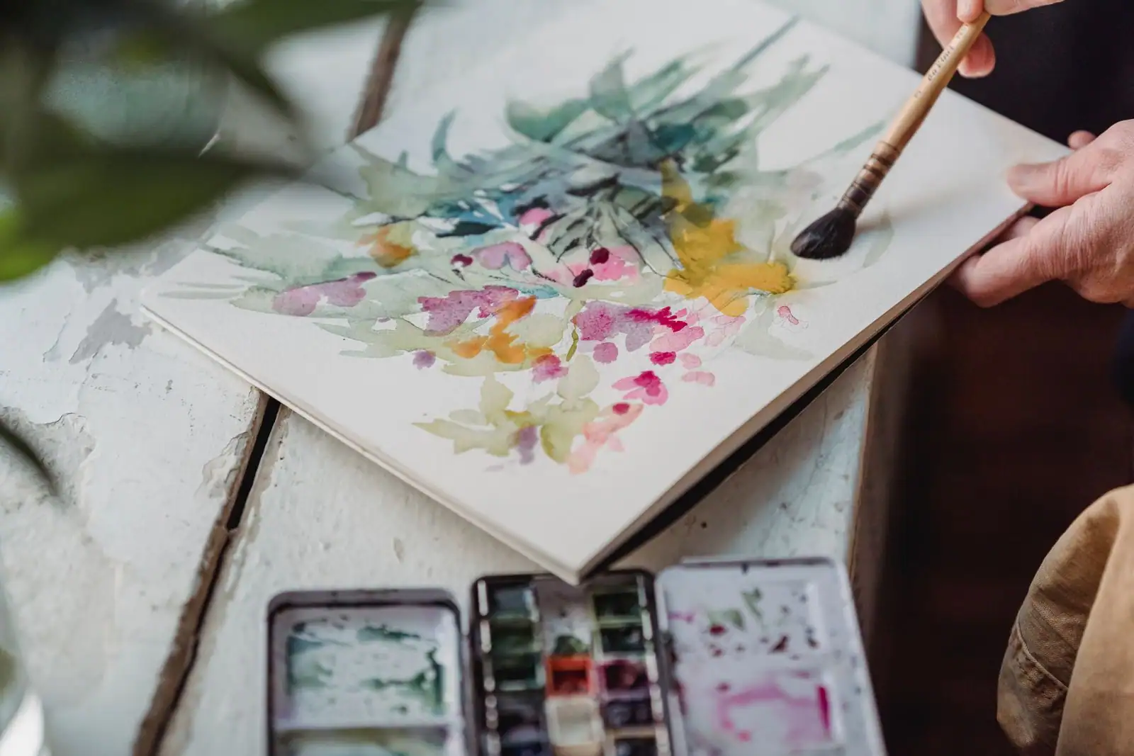 Personne peignant à l'aquarelle sur une table, matériel de loisir créatif autour