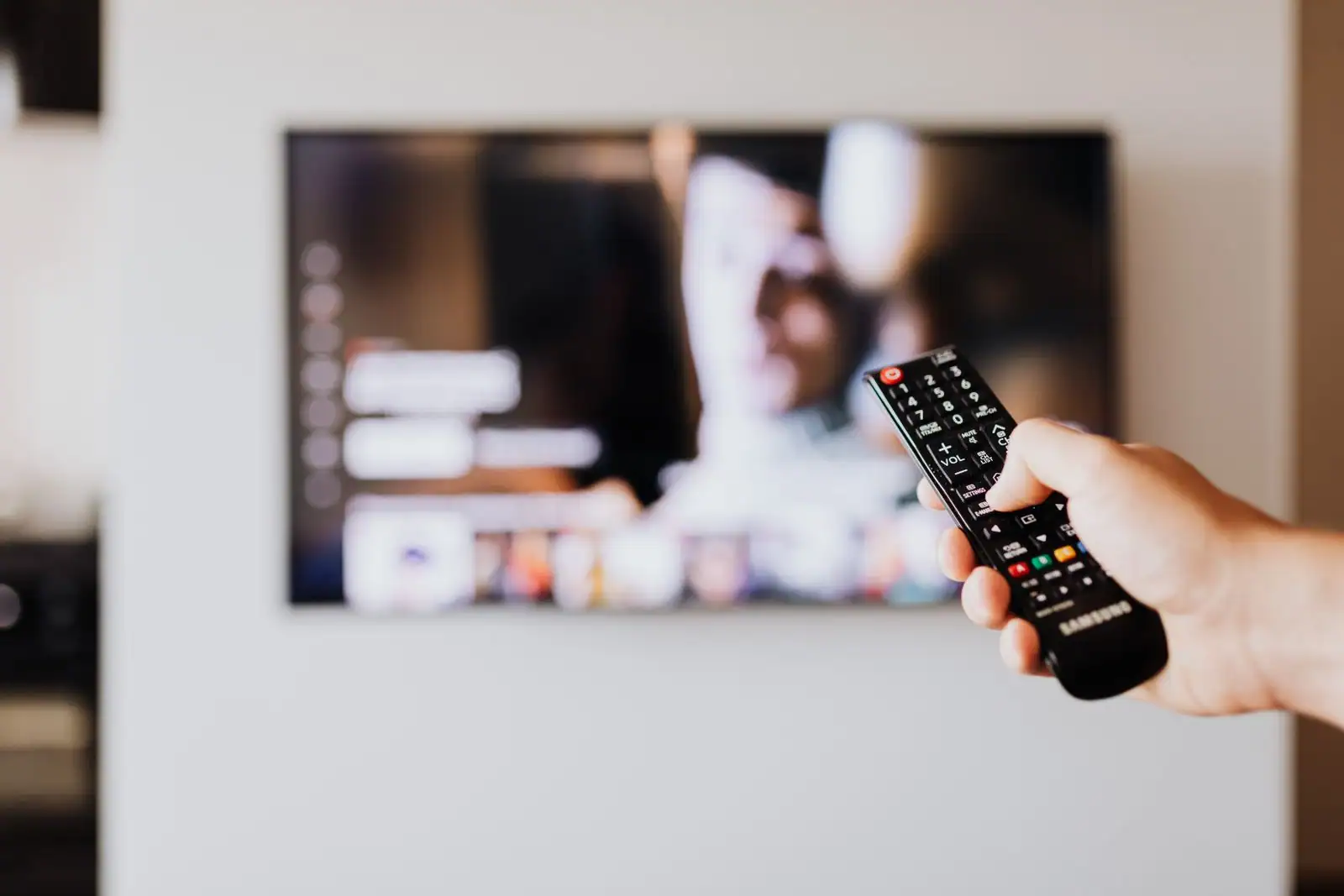 Main tenant une télécommande pointée vers un téléviseur affichant un menu de plateforme de streaming