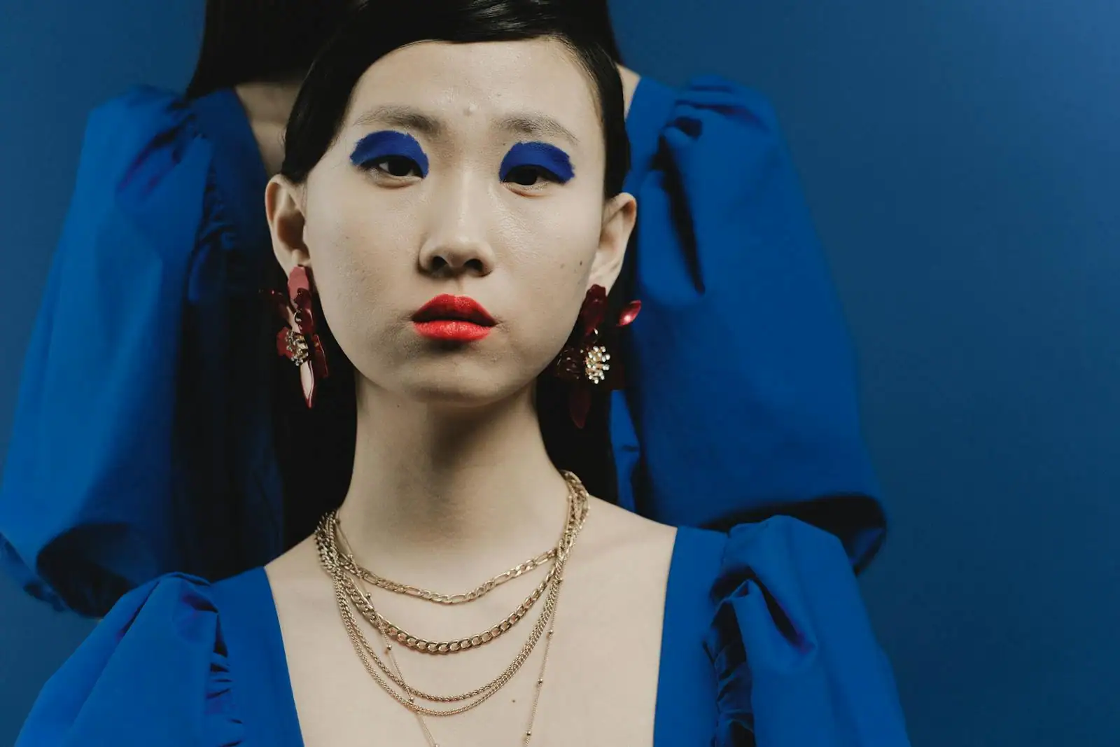 Portrait rapproché d'un visage au maquillage graphique : fard bleu vif sur les paupières, lèvres rouges et teint clair