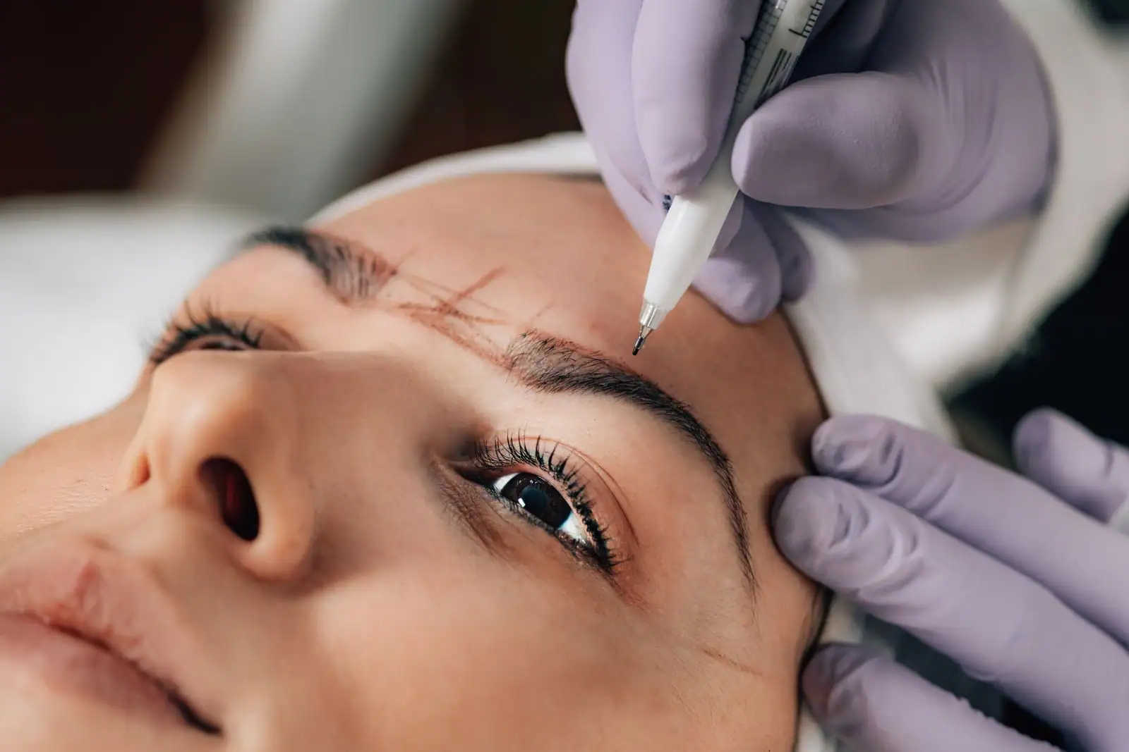 Une praticienne réalise un maquillage permanent des sourcils au microblading, en gros plan.