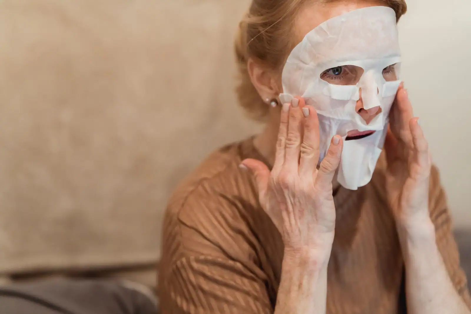 Femme appliquant un masque en tissu sur son visage des deux mains, lors d'un soin de la peau.