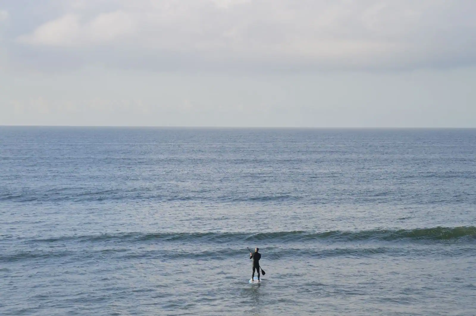 Personne pratiquant le stand up paddle sur l'océan, face à l'horizon, à l'approche d'une vague.