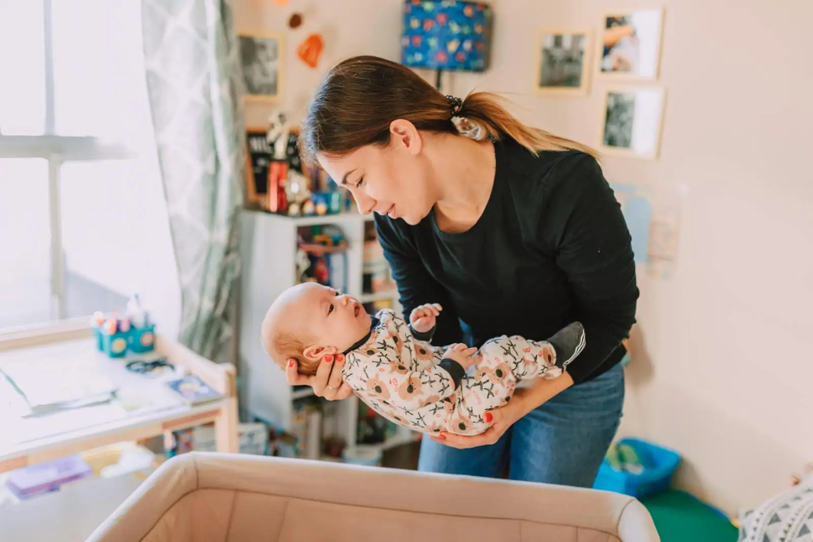 Une mère tient tendrement son bébé en pyjama au-dessus de son lit, dans la chambre
