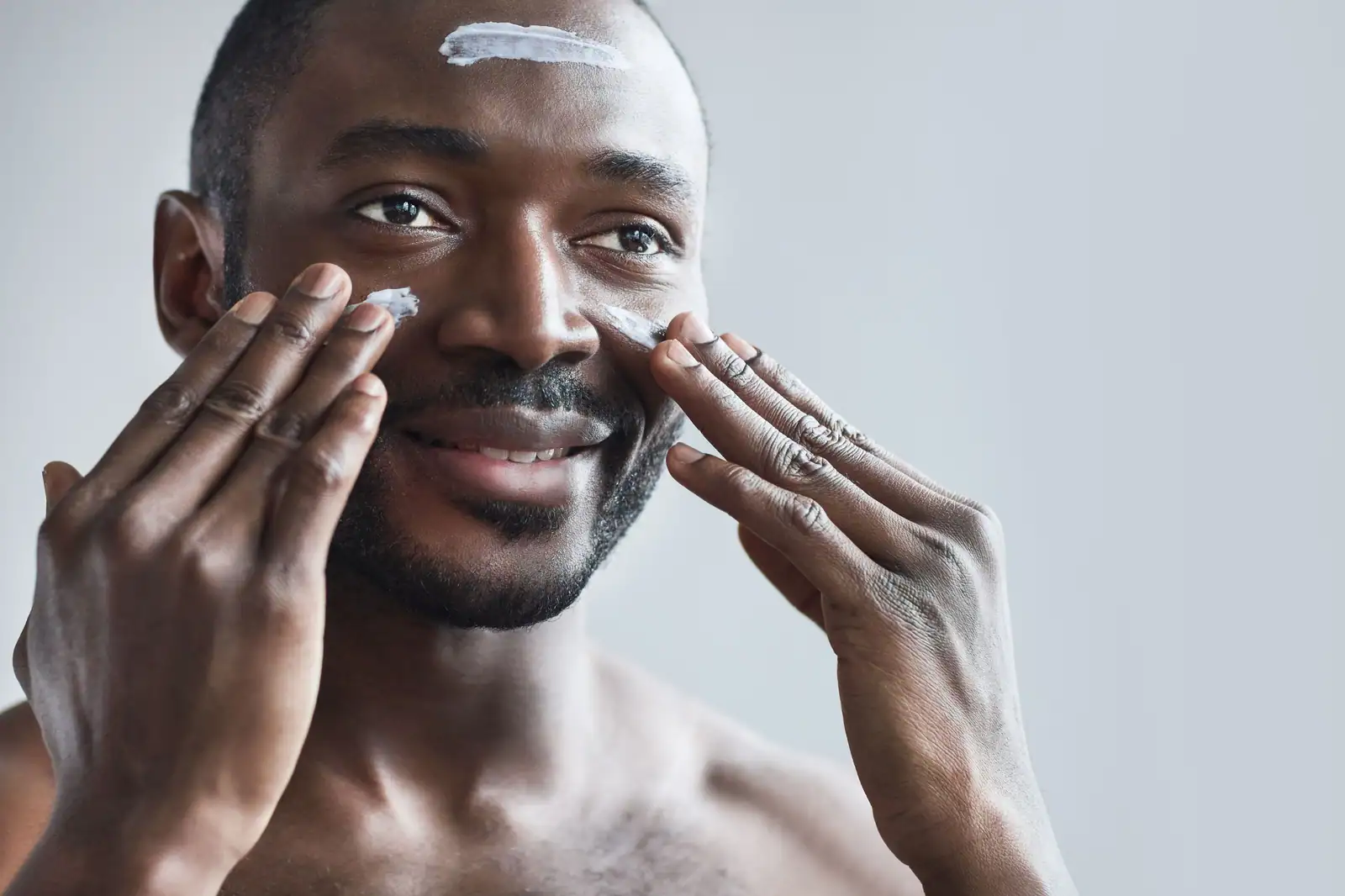 Un homme applique une crème de soin sur son visage du bout des doigts, lors de sa routine quotidienne.