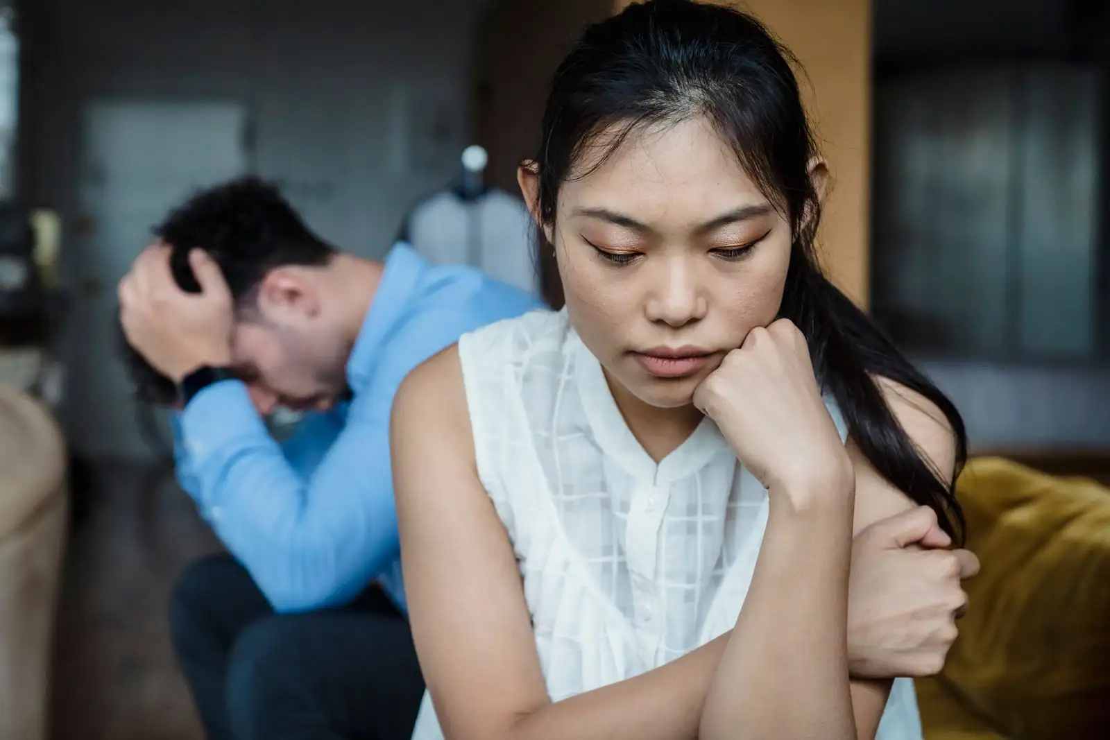 Femme pensive au premier plan, homme préoccupé en arrière-plan, évoquant une tension de couple.