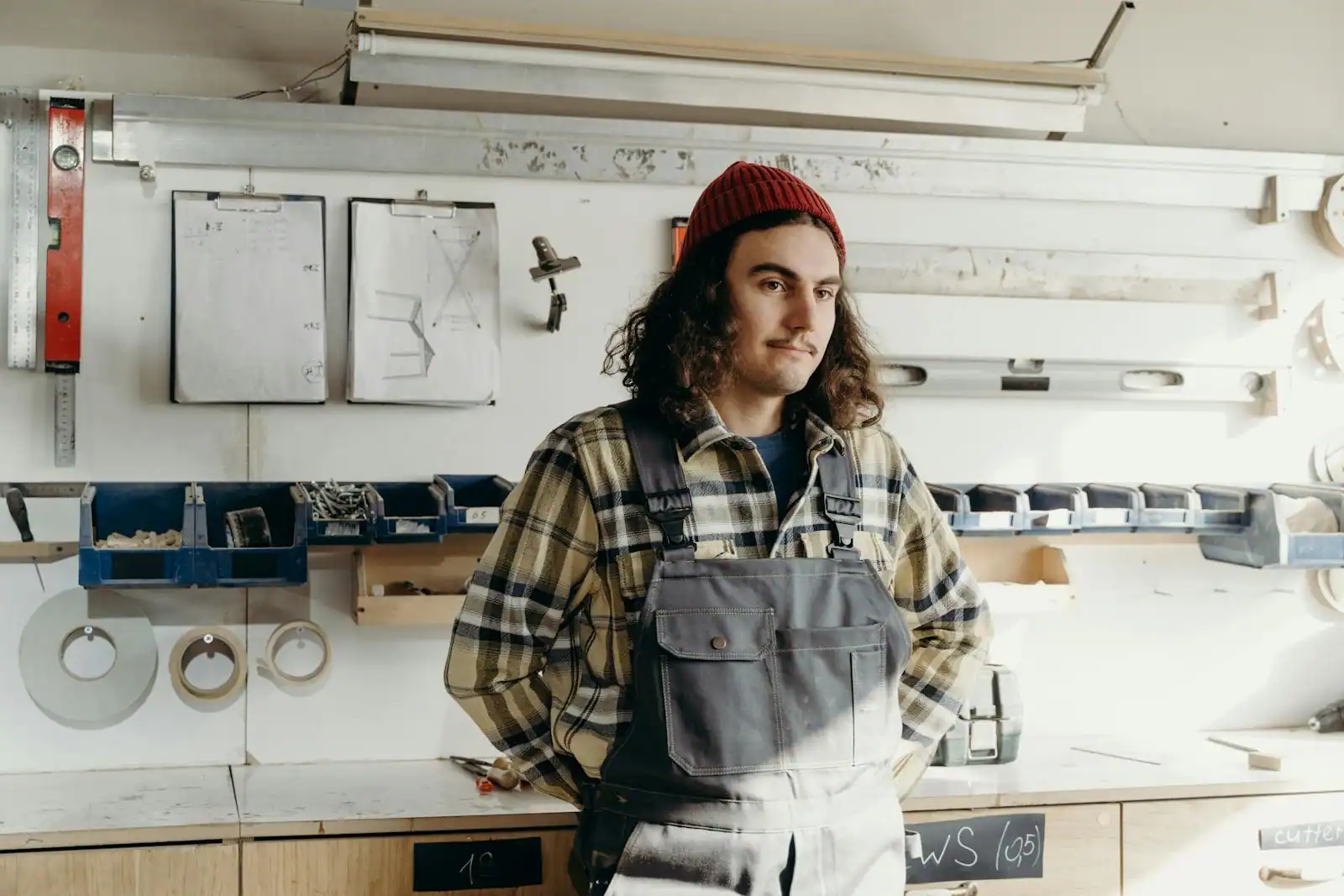 Artisan en atelier portant une salopette de travail grise et une chemise à carreaux
