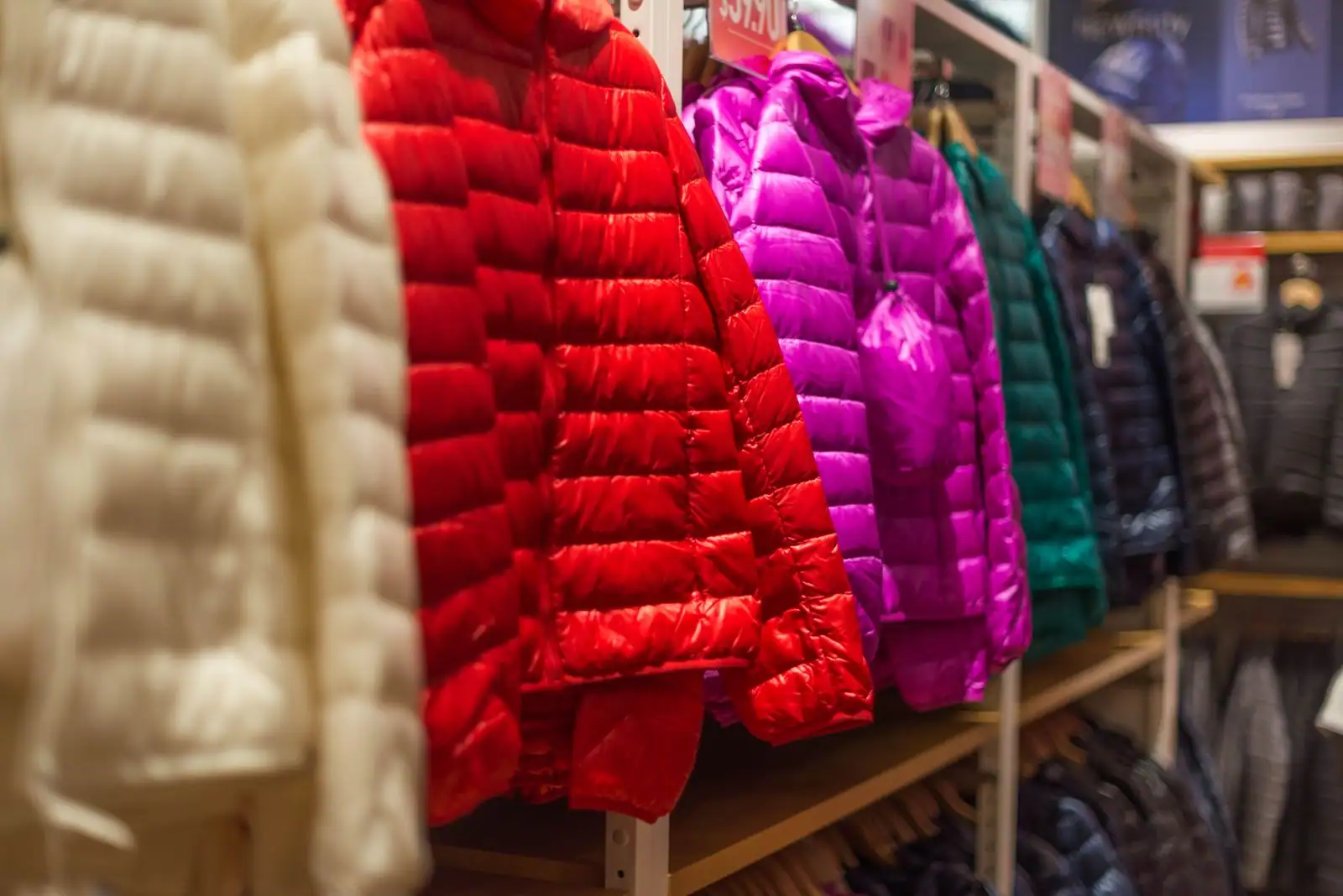 Vestes d'hiver matelassées à capuche, colorées, suspendues sur un portant en boutique