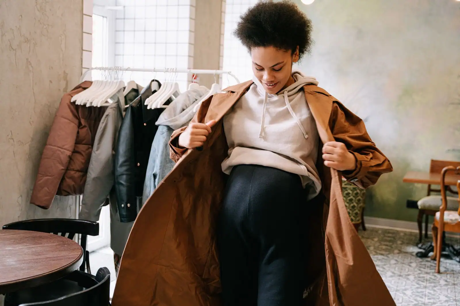 Femme enceinte essayant un manteau dans une boutique, vêtements suspendus sur un portant