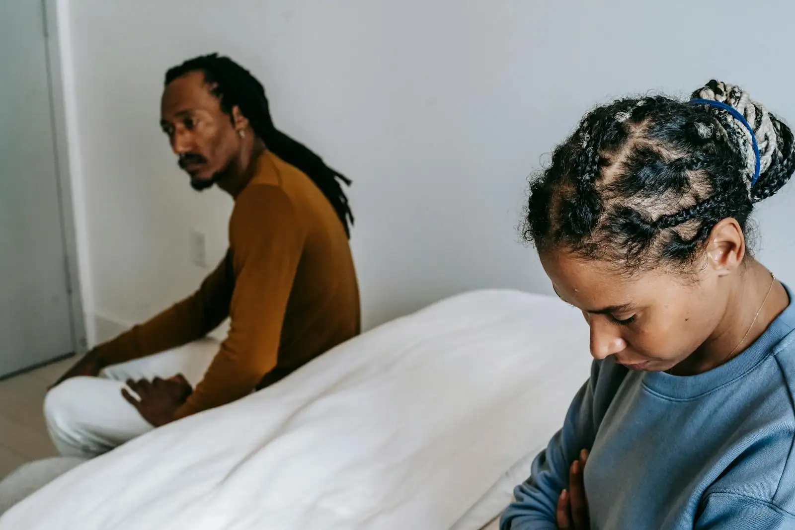 Un couple assis à distance l'un de l'autre sur un lit, le regard baissé, dans une atmosphère pensive et tendue.