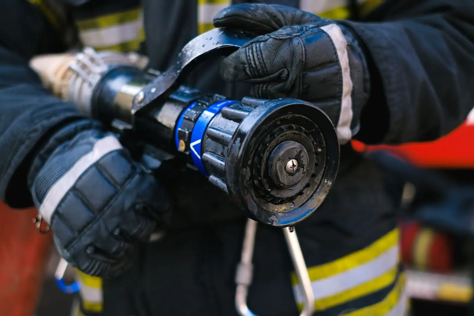 Un pompier ganté tient une lance à incendie, l’accessoire hydraulique qui règle et dirige le jet.