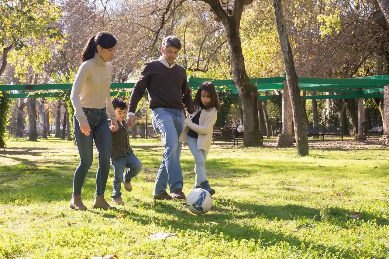 Deux parents et deux enfants jouent au ballon dans un parc, activité en plein air en famille.
