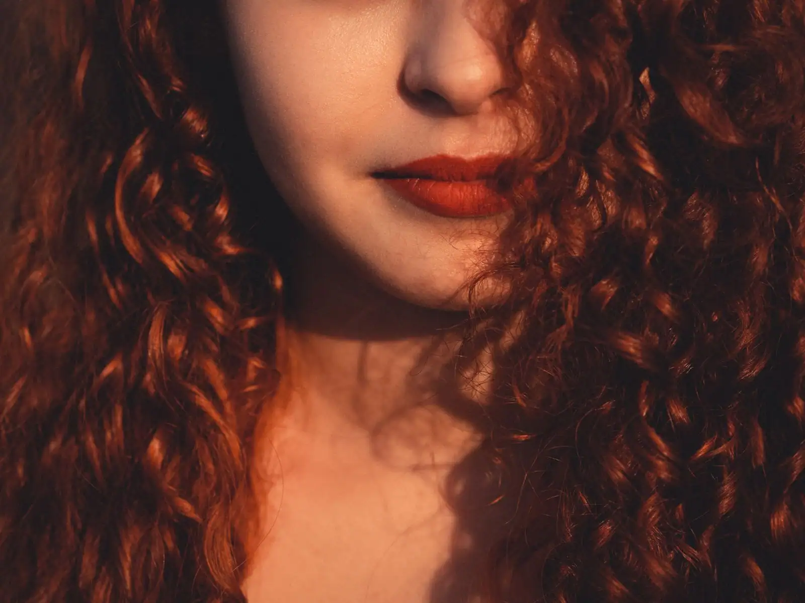 Femme aux longs cheveux bouclés acajou, un brun profond traversé de reflets rouges intenses.