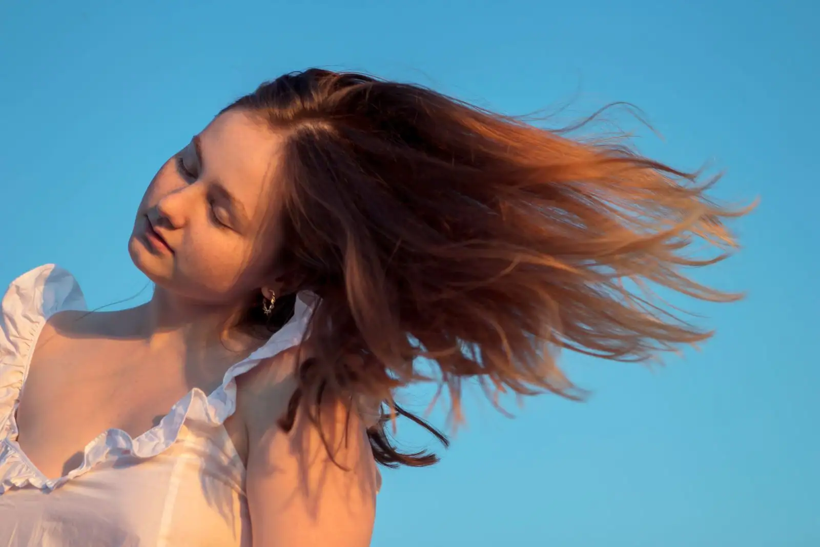 Femme aux longs cheveux châtains ondulés, soulevés par le vent et pleins de mouvement.