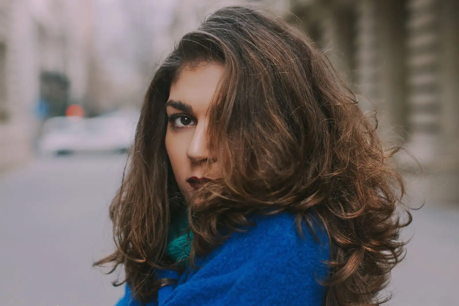 Chevelure brune volumineuse aux mèches qui se dressent et s'échappent en tous sens, en extérieur.