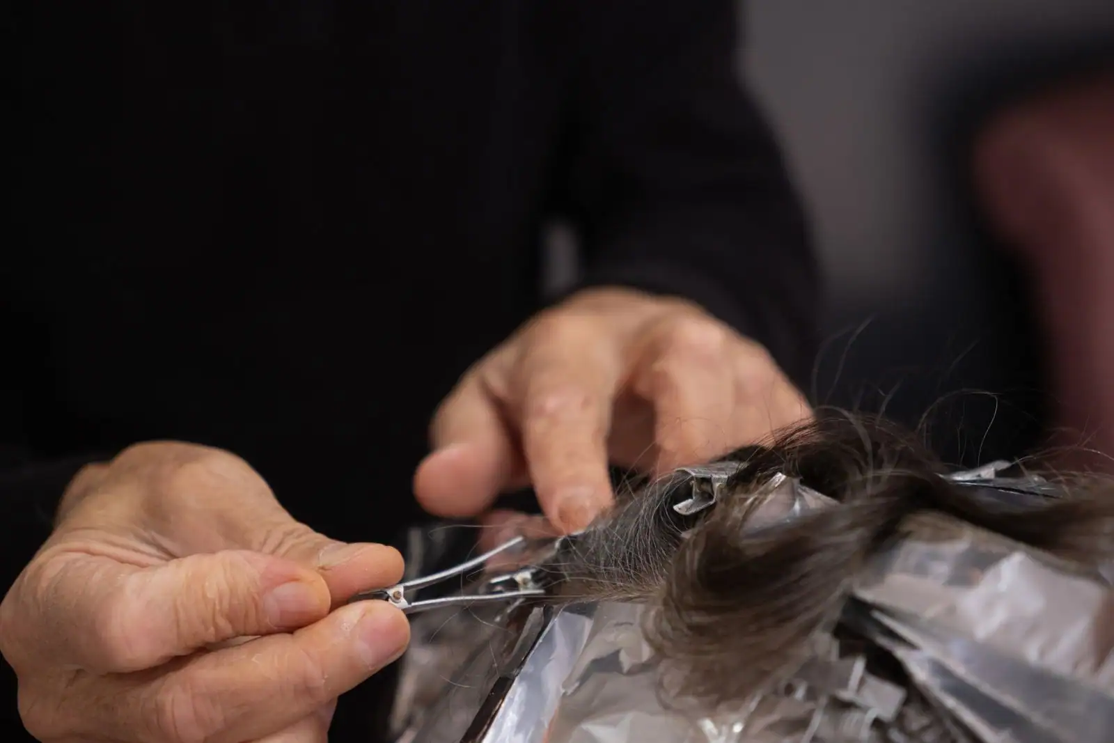 Gros plan sur les mains d'un coiffeur qui pose une mèche foncée dans une feuille d'aluminium