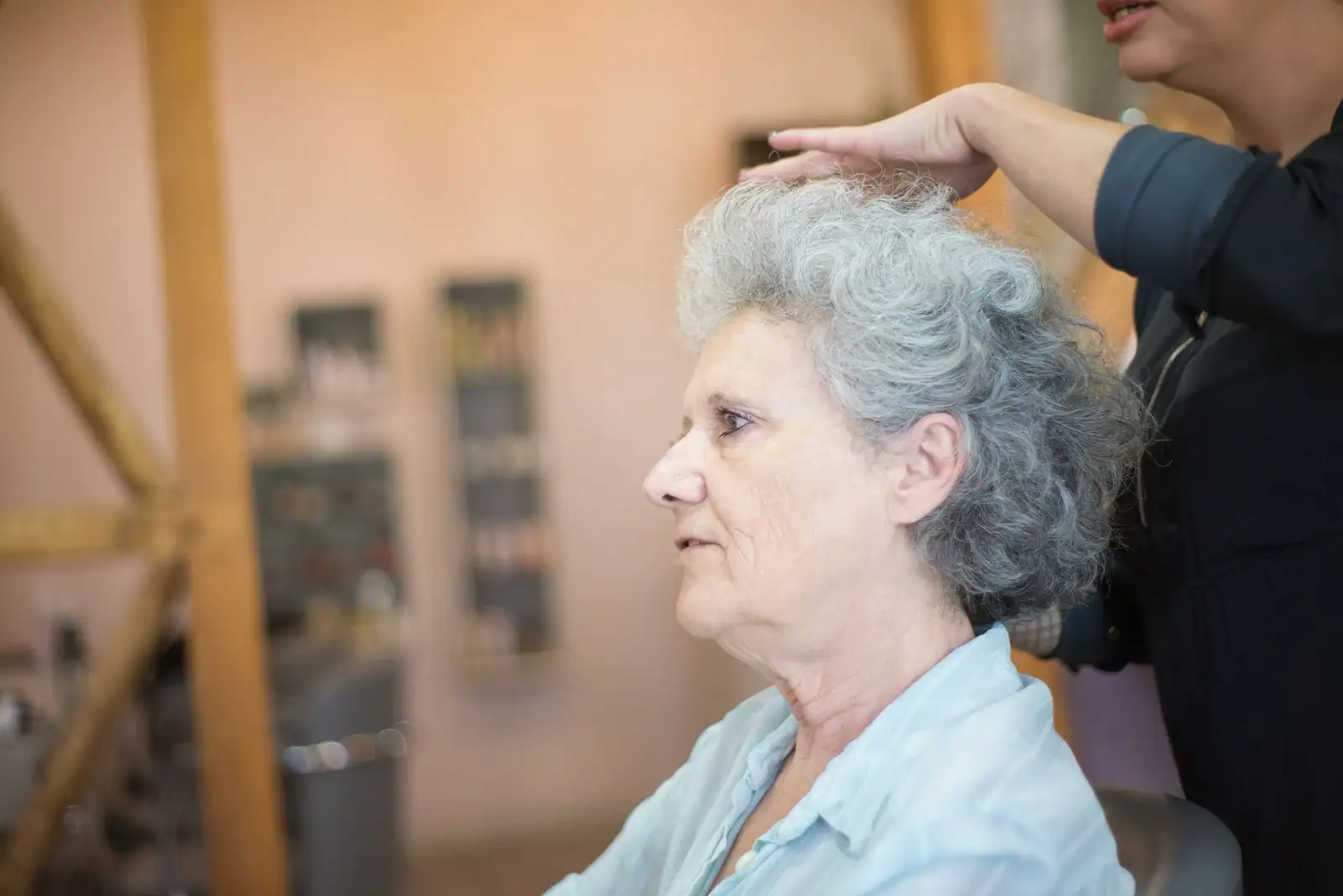 Femme âgée aux cheveux gris poivre et sel bouclés, coiffée dans un salon de coiffure.