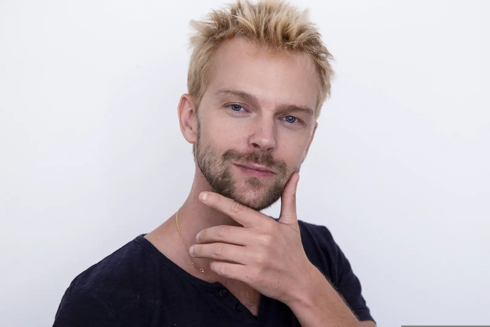 Un homme aux cheveux courts éclaircis dans un blond doré, la barbe restée plus foncée, sur fond clair.