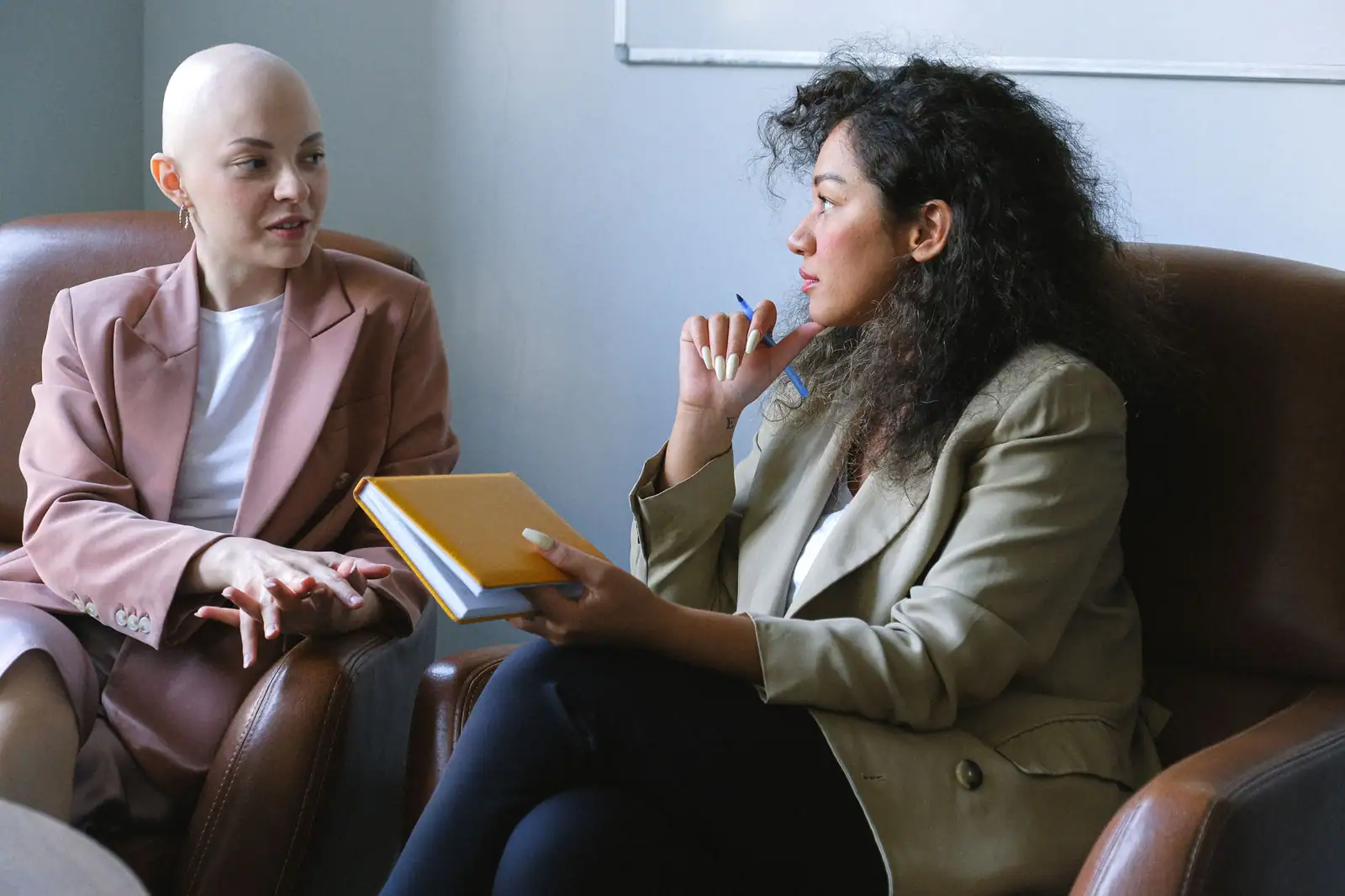 Deux femmes assises face à face dans des fauteuils, l'une parlant, l'autre écoutant, carnet en main