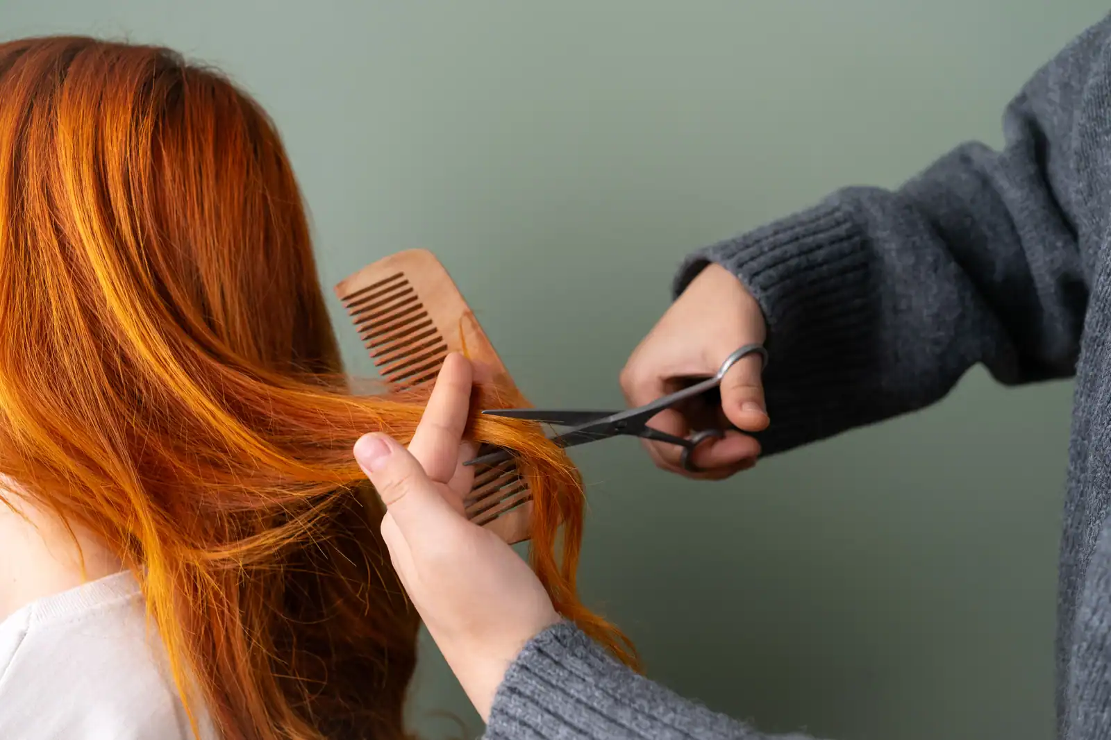 Mèche de cheveux longs pincée entre les doigts et coupée aux ciseaux de coiffure, peigne à la main
