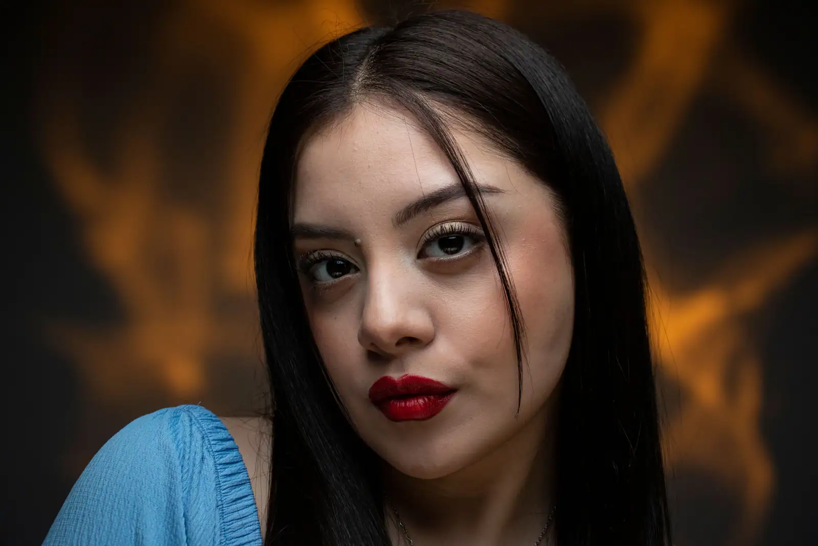 Portrait rapproché d’une femme aux longs cheveux noirs et à la bouche rouge saturée, peau laissée dans sa nuance.