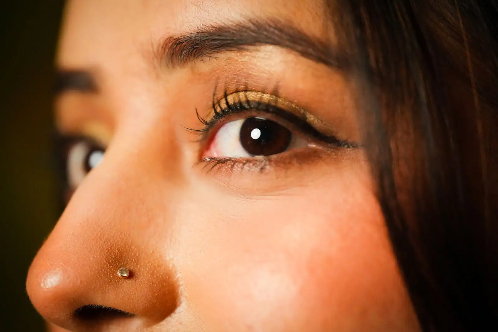 Gros plan sur un œil féminin maquillé d'un fard doré et d'un liseré sombre le long des cils, en lumière chaude.