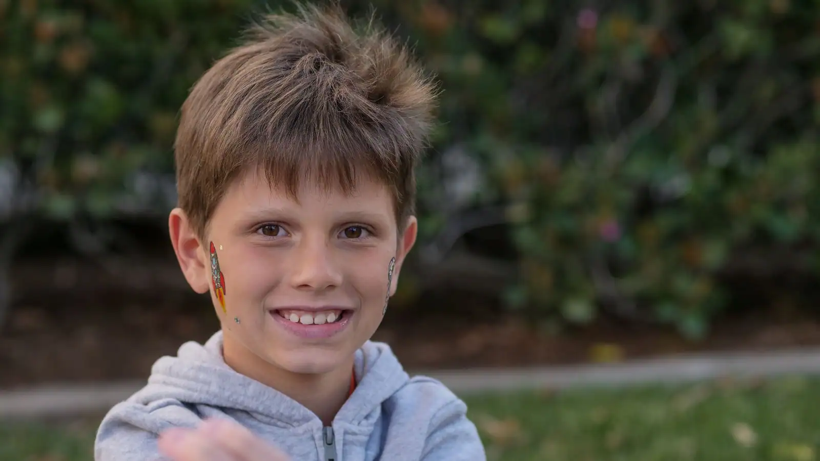 Jeune garçon souriant avec de petits motifs colorés peints sur les joues, dont une fusée, exemple de maquillage enfant.