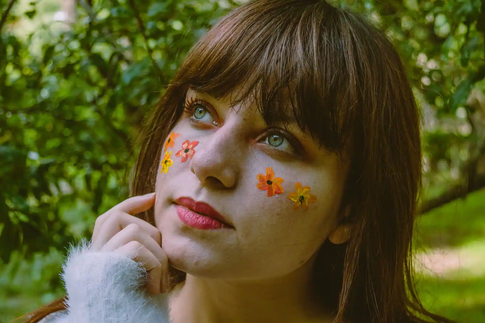 Visage à la peau nue et aux taches de rousseur, petites fleurs peintes sur les pommettes, en extérieur.