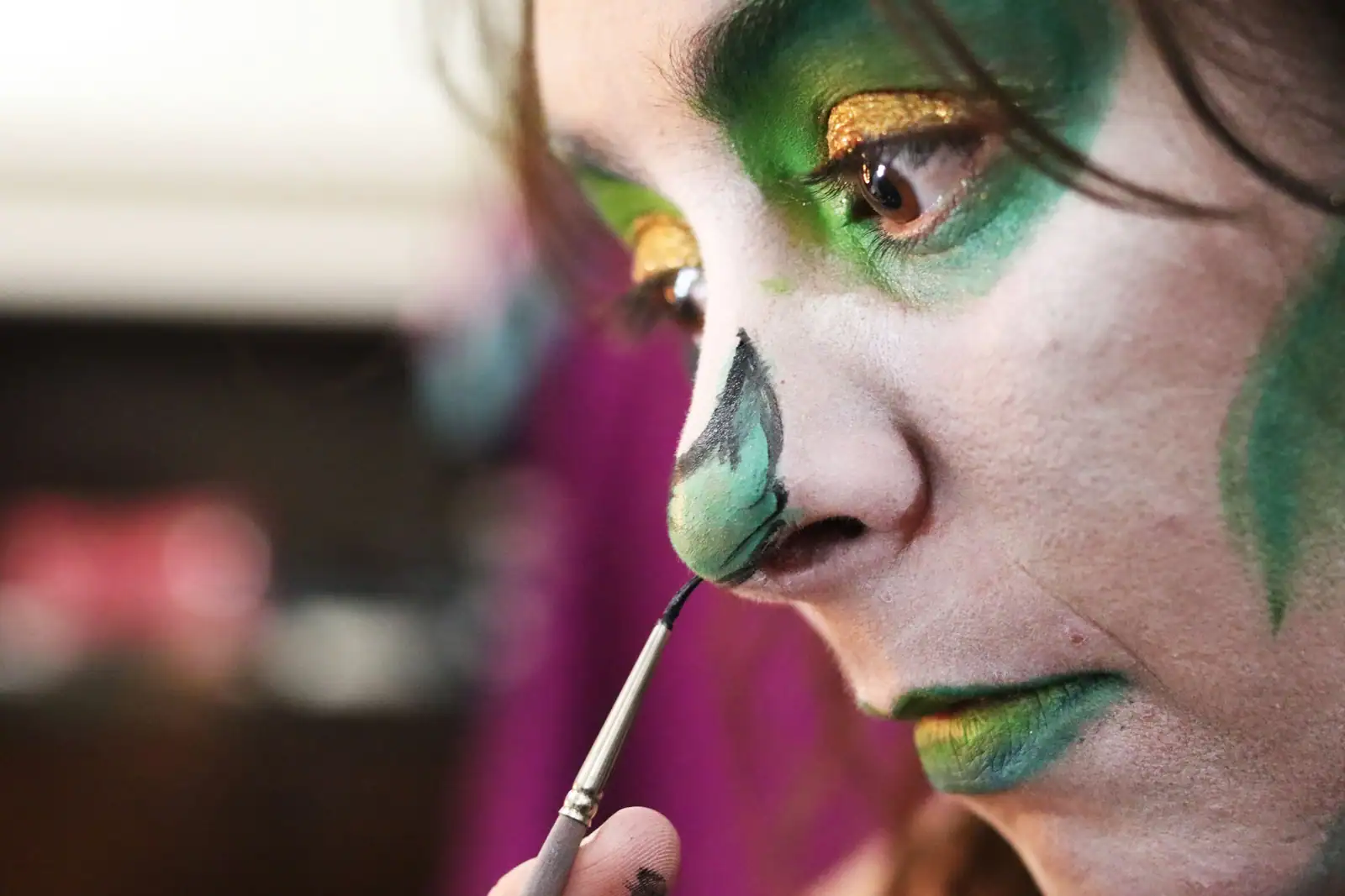 Application au pinceau de peinture verte sur un visage, gros plan d'un maquillage de déguisement.
