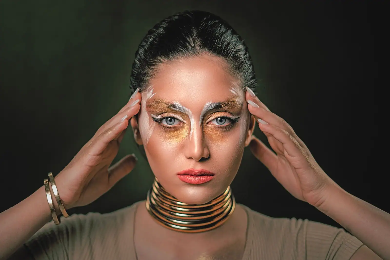 Maquillage doré métallique posé en masque autour des yeux, souligné de fins filets blancs.