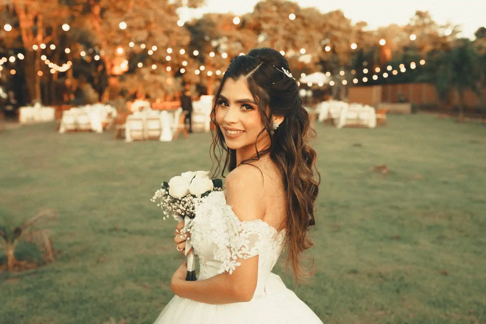 Une mariée en robe blanche tient son bouquet dans un jardin, à la lumière chaude de fin de journée.