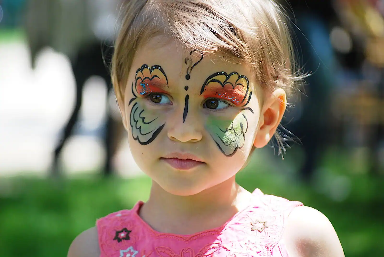 Visage de petite fille maquillé en papillon, ailes orange et vertes déployées autour des deux yeux